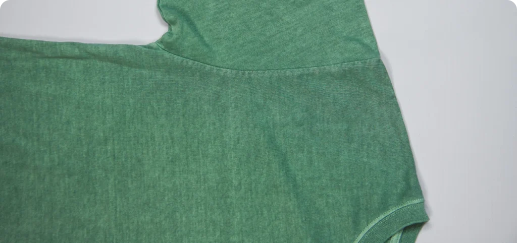 Close-up das costuras da t-shirt verde, destacando a malha e o acabamento da Rotex.