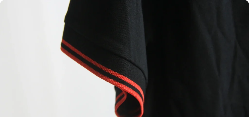 Detalhe da manga de polo azul escuro com riscas vermelhas no punho